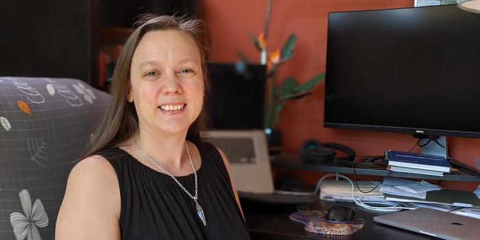 a person with long hair smiling while sitting in front of a desktop computer