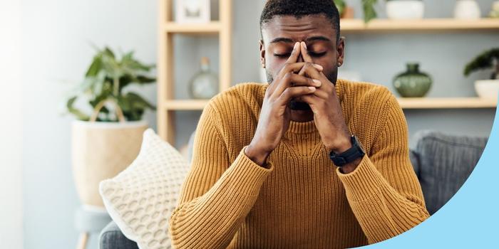 person sitting on a couch with their hands to their face and eyes closed, upset