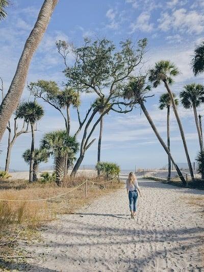 author April Zimmerman seen from behind walking on a sand path toward the beach with trees rising up on either side