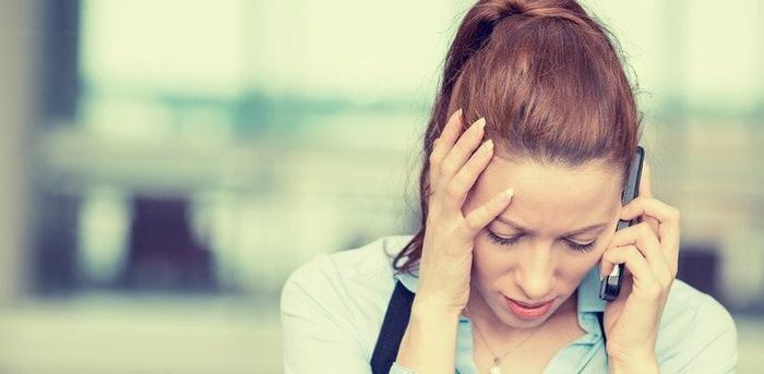 person holding a cell phone to their ear with one hand and holding their face with the other