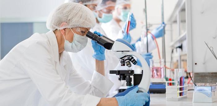 Scientists wearing protective gear looking through microscope