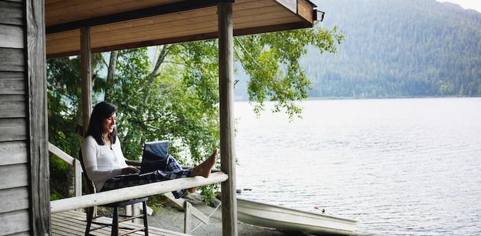 person working on laptop on deck next to a lake