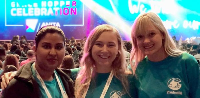 3 women wearing Prudential T-shirts with a sign saying "Grace Hopper Celebration" in the background