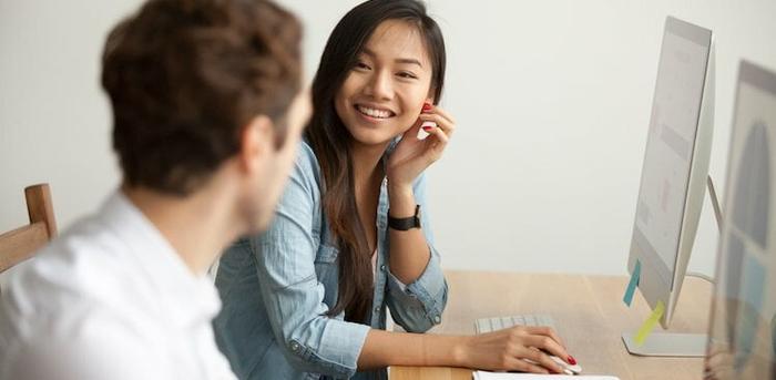 intern working on a desktop computer and talking with a peer