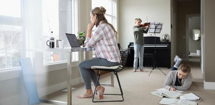 parent at computer with two kids in background courtesy Hero Images/Getty Images