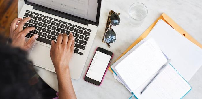 person typing on laptop at table with papers on it