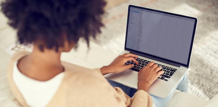 person sitting on couch typing on laptop viewed from behind