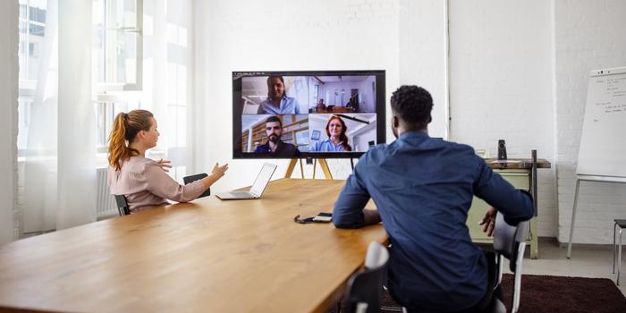 two people in conference room on video call with rest of their team