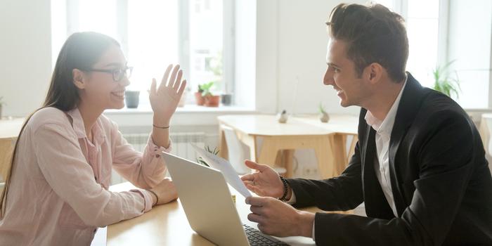 two people talking excitedly at job interview, sitting at table with laptop, one person holding resume