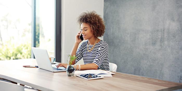 woman sitting at a desk while using a computer and talking on the phone