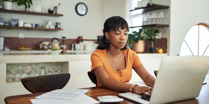 person at kitchen table with laptop and papers