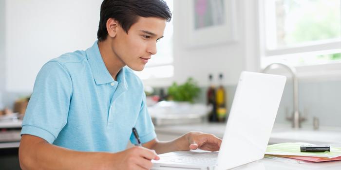 young person at kitchen table with paper and laptop