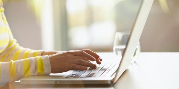 person's hands typing on laptop resting on table next to glass of water