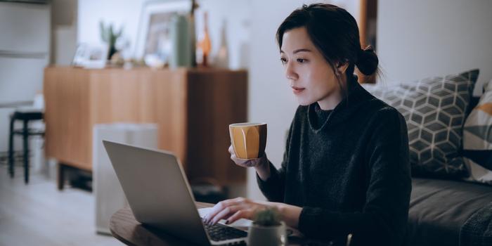 person working at laptop on coffee table while sitting on the floor holding a mug