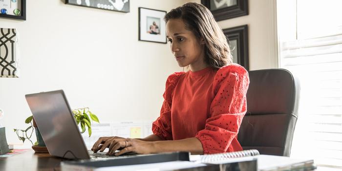 person sitting at desk in home office, typing on laptop