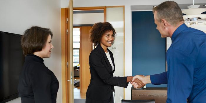 two people shaking hands in office with third person watching