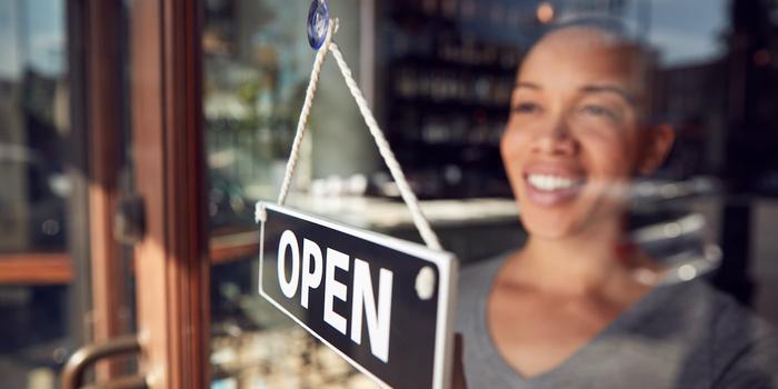 person looking through a window hanging an "open" sign