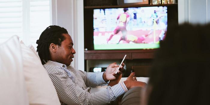 person watching a soccer game on TV and looking at their phone