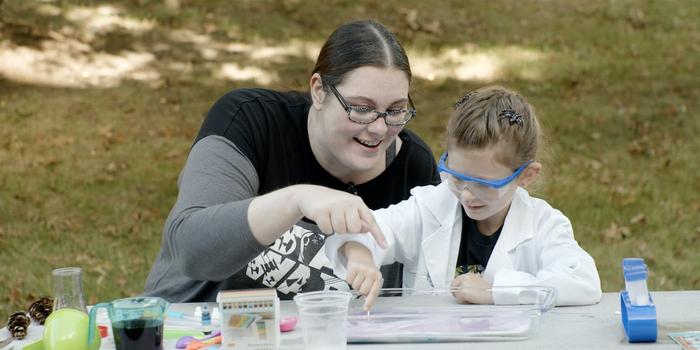 a person and a child sitting at a table outside doing a science project