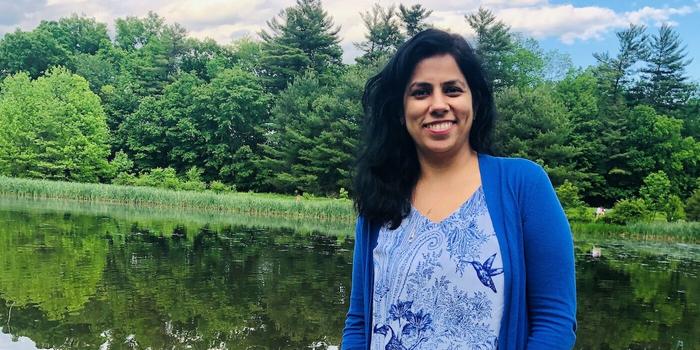 person with long dark hair standing in front of a lake and trees