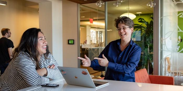 Two people smiling while sitting together with a laptop in an office