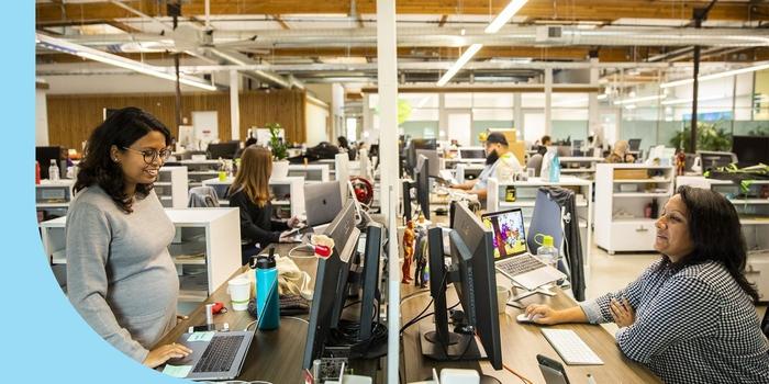 Two Clover employees smiling and talking across from their desktop’s in the office.