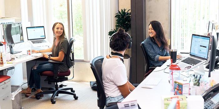 three people chatting from their desks in an open plan office