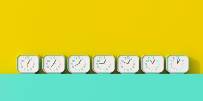 line of teal analog clocks set to different times on a teal surface against a yellow wall