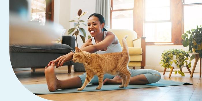 A woman stretching her legs on a yoga mat while exercising at home with her pet cat.