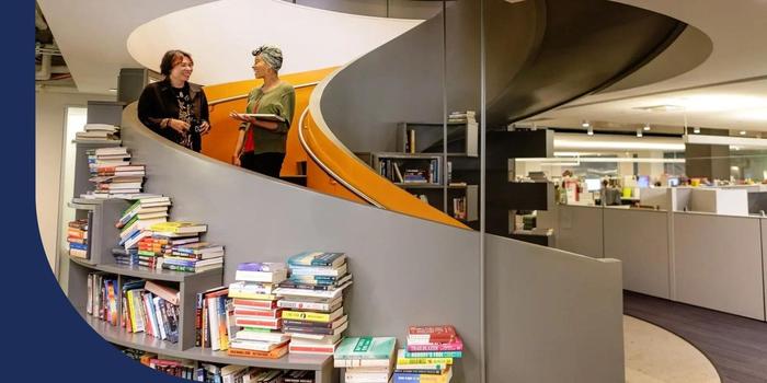 Two Hachette Book Group employees talking while doing down a spiral stairway in the office.