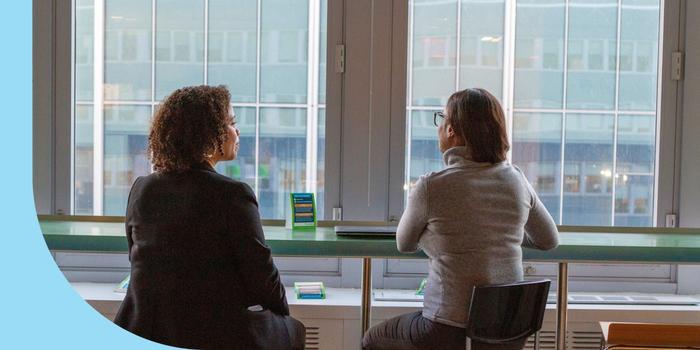 Two Healthfirst employees in discussion while sitting and facing the window.