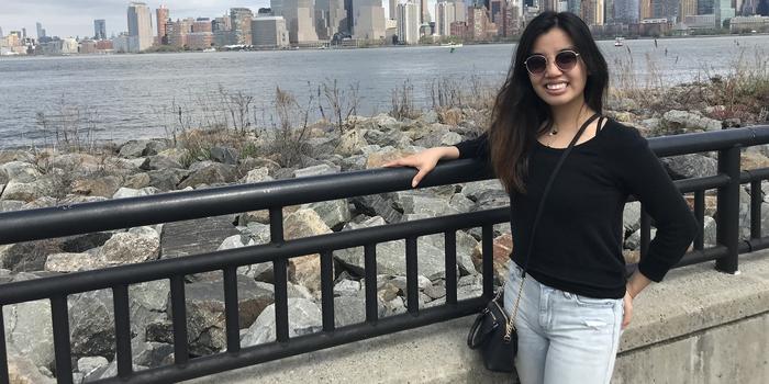 person with long hair wearing sunglasses standing with the New York City skyline in the background