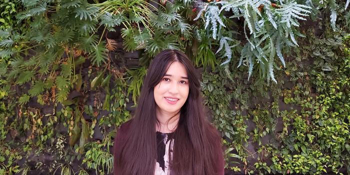 person with long brown hair standing in front of a wall of plants