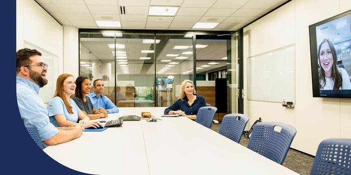 A group of coworkers gathered on one side of a conference room table while having a virtual meeting with a remote colleague.