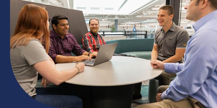 Five Stryker employees sitting around a table laughing while one types on a computer.