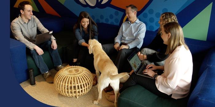 Upside employees sitting on a couch and petting a dog in the office.