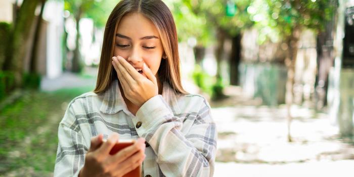 person walking down the sidewalk, looking at red phone in their hand and gasping with their hand over their mouth