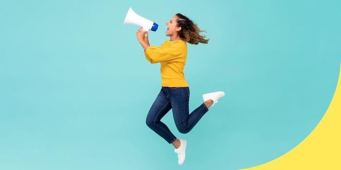 side view of a person dressed in blue jeans, a yellow sweater, and white tennis shoes jumping in the air and yelling through a megaphone