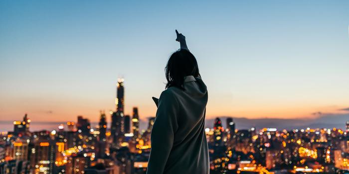 person standing over a large city at dusk, facing away from the camera, pointing at the sky