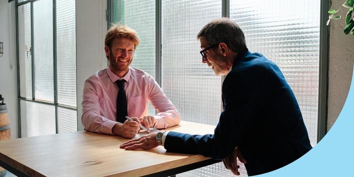 two people sitting at a table talking during a job interview with a frosted class window in the background