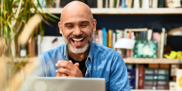 person sitting in front of bookcase, looking at laptop and smiling