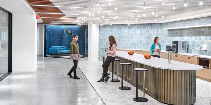 Employees in an office kitchen area with an island and barstools.