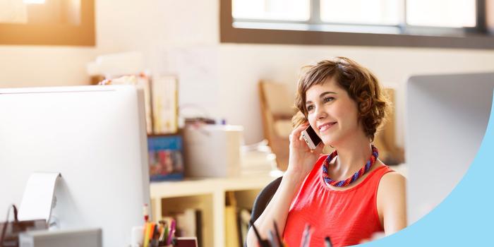 person sitting at desk looking at computer screen and talking on a cell phone