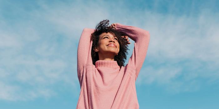 person smiling with arms raised in front of partly cloudy blue sky