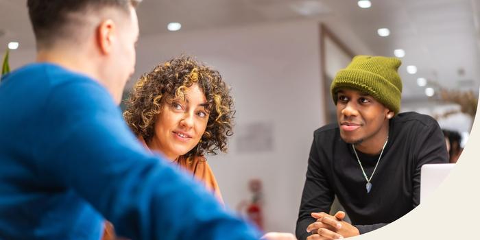 three people standing around a table discussing work in an office with white walls