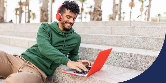 person sitting on concrete steps outdoor typing on an orange laptop and smiling