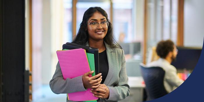 a person walking through an office, smiling and holding folders