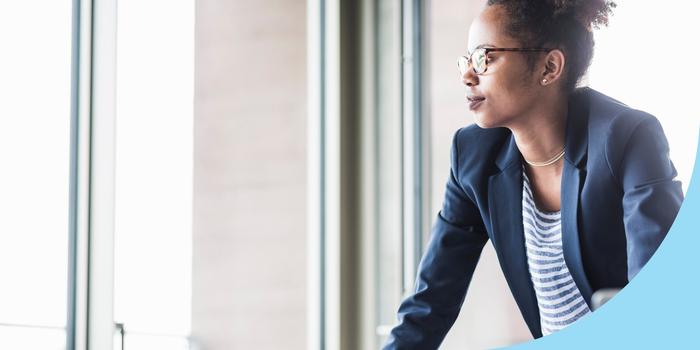 person in office leaning on desk and looking out window