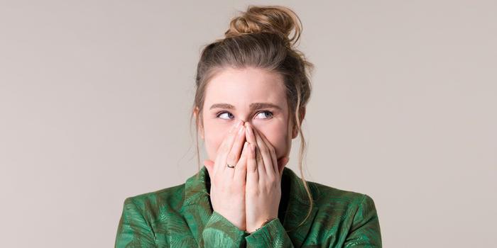 person holding hands over their face and looking off to the side like "oops!" wearing a green top against a beige background