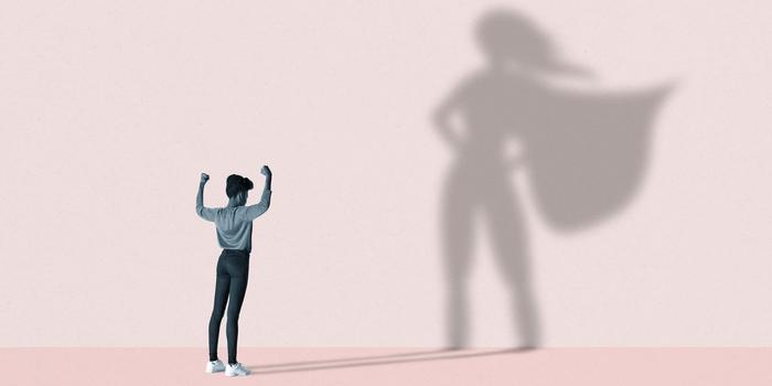 person standing with their hands up against a pink wall casting a shadow in a superhero pose